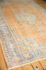 Distressed Oushak rug corner with faded tangerine field, royal blue border, and textured wear.