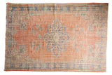 Distressed Oushak carpet with faded terracotta, blue medallion, and Rococo palmettes.