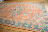 Corner of distressed Oushak rug, pale red field, blue border, Rococo details, even wear.