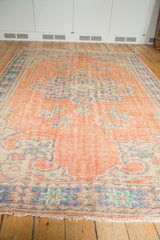 Vintage Oushak carpet's fringed edge, distressed pale red pile, and blue Rococo border motifs.