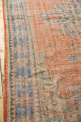 Distressed Oushak carpet side, worn pale red pile, sky blue motifs, visible foundation.