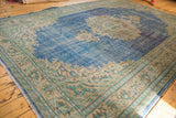 Vintage distressed Oushak rug corner, showing worn blue field, patterned beige border, and fringe.