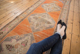 A vintage Oushak runner with a column of distressed medallions on an abrashed tangerine orange field.