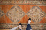A personal perspective looking down at the distressed texture and tangerine field of a vintage Oushak runner.
