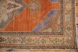 A distressed Oushak rug corner with a tangerine field, scrolling details, and beige and brown geometric borders.