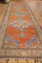 A low angle view along the length of a distressed Oushak runner showing its tangerine orange field.