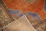 Folded corner of a distressed Oushak rug showing the hand-knotted foundation and low tangerine pile.