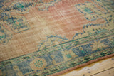 Distressed vintage Oushak rug, worn blush field, faded royal blue motifs, exposed foundation.