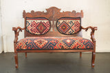 Intricately carved vintage wood bench with vibrant red, blue, and cream geometric Kilim upholstery.