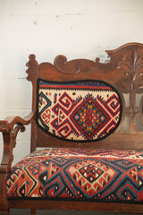 Carved backrest of a vintage bench with vibrant geometric Kilim upholstery.