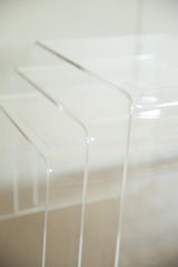 Clear Lucite nesting tables stacked, revealing transparent edges and subtle surface scratches.