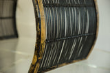 Curved side view of vintage black rattan foot stool, highlighting woven texture and chippy paint.