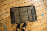 Curved frame and chippy black paint detail of vintage rattan foot stool.