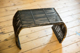 Curved leg of vintage black rattan foot stool showing chippy paint finish.