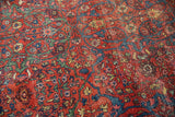 Intricate madder red floral motifs and green arabesque vines on a worn antique Fereghan carpet.