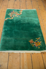 Intricate blush, gold, and blue floral motif on emerald green Art Deco rug corner.
