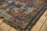 Distressed corner of an antique Caucasian rug, showing exposed foundation, geometric border, and tattered fringe.