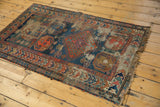 Geometric border patterns, worn blue field, and tattered fringe on an antique Caucasian rug.