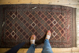 Antique Belouch rug corner, featuring geometric lattice with inverted fills in wine red and ivory hues.
