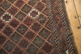 Detail of antique Persian Belouch rug's lattice pattern, with wine red, charcoal tones, and secured edge.