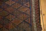 Antique Belouch rug detail: navy, madder root red geometric medallions, and intricate pawn design border.