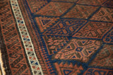 Close-up of antique Belouch rug's navy, red, and ivory geometric patterns with pawn design border.