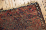 Antique Belouch rug texture showing geometric starburst gul, dark blush, navy, brown, and visible wear.