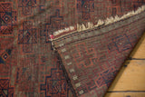 Antique Belouch rug showing geometric motifs, hand-knotted reverse weave, and aged fringe.