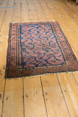 Persian Belouch rug corner highlighting repeating navy gul motifs, chestnut hues, and geometric border.