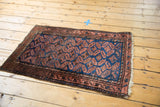 Belouch rug corner detail, showing navy pinwheel gul motifs, chestnut border, and secure fringe.
