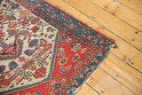 Tattered corner of antique Malayer fragment rug, showing red, blue borders, and ivory field.