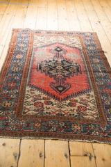 Vintage Kurdish Malayer rug corner showing blue floral border, blush red field, and light tatter.
