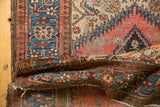 Folded vintage Malayer rug with intricate borders, serpentine motifs, and soft red, blue tones.