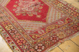 Vintage Melas rug corner with cherry red borders, saffron floral motifs, and visible tattered fringe.