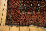 Tattered end and low pile of antique Belouch runner, highlighting brick red starburst border.