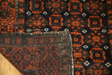 Antique Belouch rug corner showing hand-knotted weave, dark red geometric motifs, and original selvage.