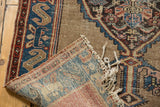 Antique Malayer rug corner showing woven foundation, blue geometric border, and tattered fringe.