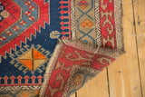 Folded corner of antique Caucasian rug showing geometric border, tattered fringe, and hand-knotted foundation.