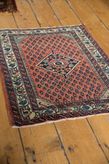 An angled view of a vintage Persian Engelas rug, showcasing its brick red boteh field and navy diamond medallion.