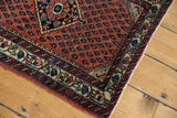 Corner detail of a vintage Persian rug's brick-red boteh field next to its colorful ivory border.