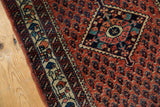 Detailed corner of a vintage Persian rug with a navy diamond medallion over a brick red boteh field.