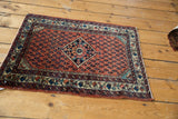 Angled view of a vintage Persian Engelas rug mat showing the boteh field and central medallion.