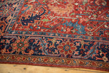 Antique Heriz carpet: Geometric navy blue border, cherry red field with scrolling motifs.