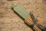 Close-up of sage green square beeswax taper candles in cardboard wrap with branded ribbon.