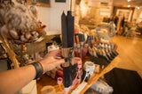 Hand holding square black beeswax taper candles with brown corrugated band and ribbon.