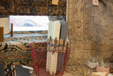Bundled cream and dark grey beeswax square taper candles in a red wire basket.