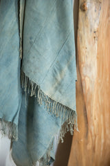Vintage African indigo textile with soft denim blue tones, diagonal stitching, and fringed edge.