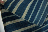 Supple, folded hand-woven African indigo textile featuring varied blue and natural stripes.