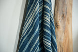 Draped vintage African indigo textile with varied blue stripes and hand-woven texture.