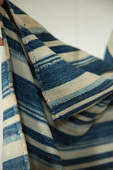 Folded hand woven vintage African indigo textile showing varied blue stripes, natural tones, and visible panel joins.